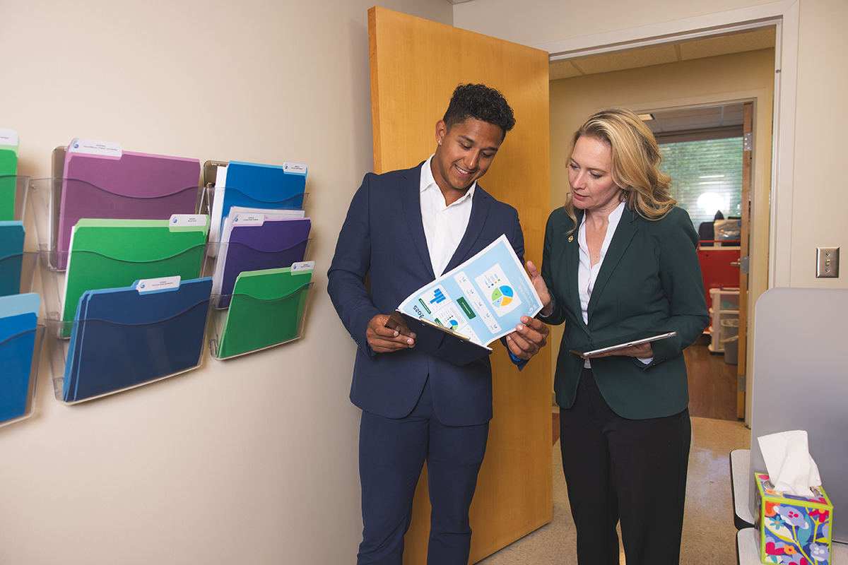 Two people look at papers on a clipboard in a medical office.