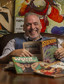 Dr. David Earle sitting in a chair in his office reading comic books.