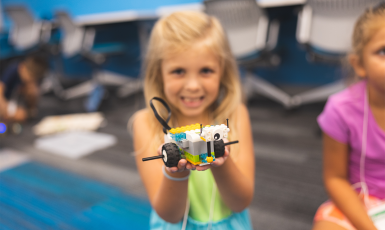 Smiling child holds a small lego car in her hands.