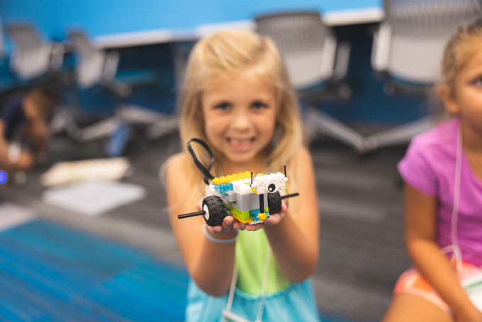 Smiling child holds a small lego car in her hands.