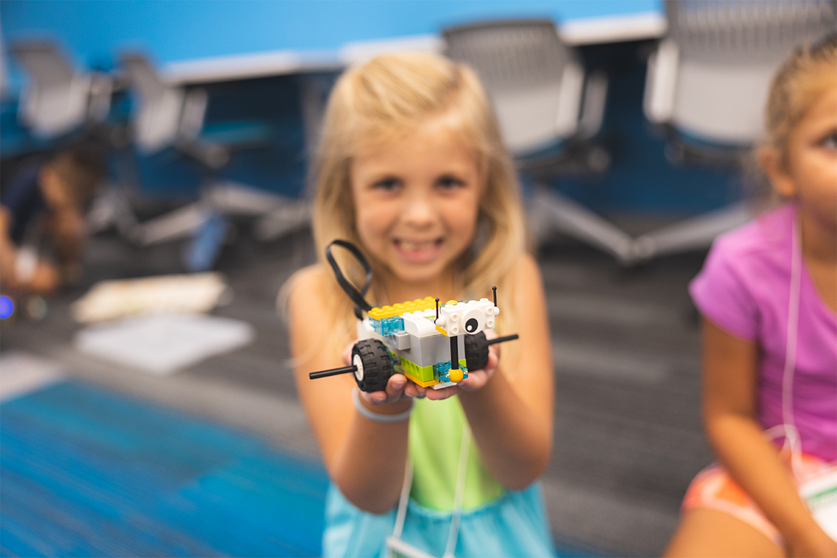 Smiling child holds a small lego car in her hands.