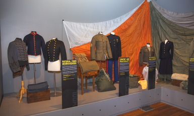 Seven different military uniforms in a museum display.