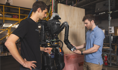 Two people look at a life-sized humanoid robot in a lab.