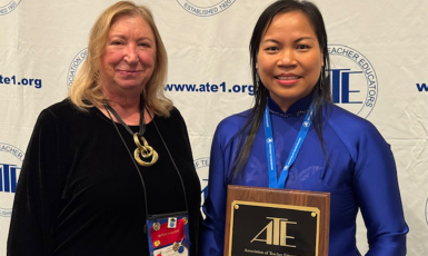 Two people stand side by side, the person on the right holding a plaque award in front of her body.