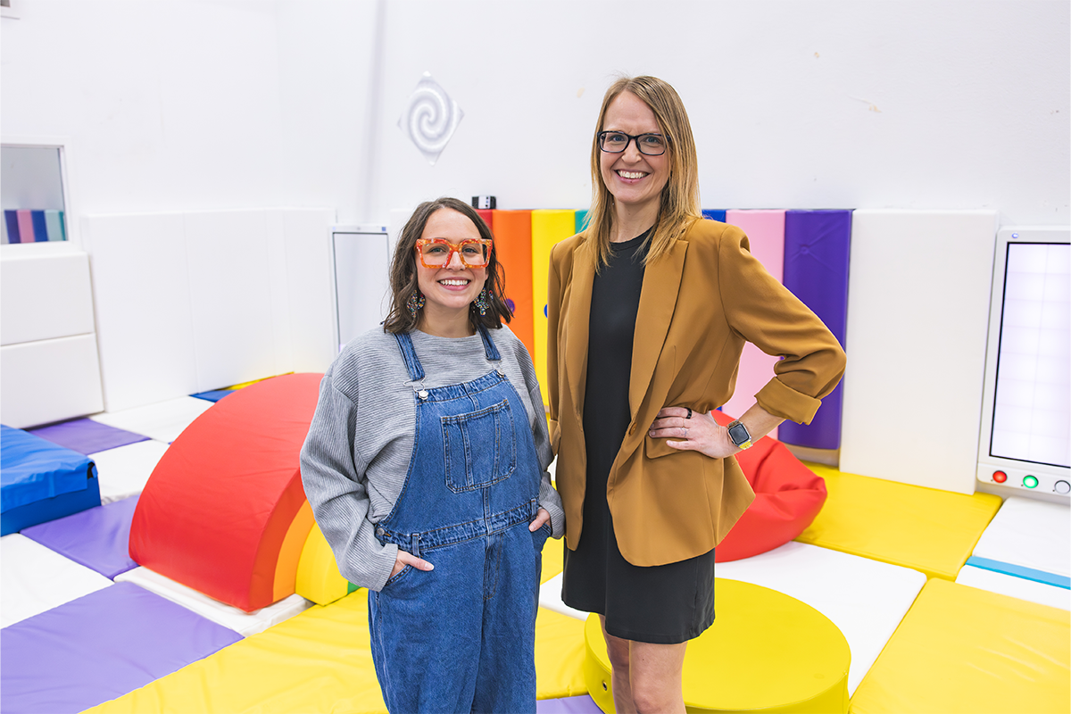 Two special education specialists stand in a room with colorful mats.