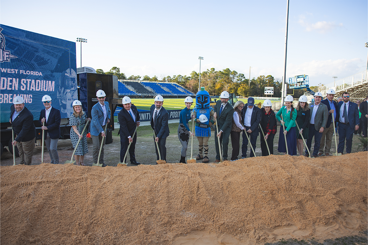 16 people and the Argonaut mascot hold shovels at the stadium groundbreaking