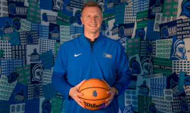 Basketball coach holds basketball in hands in front of a collage wall with Argo graphics.
