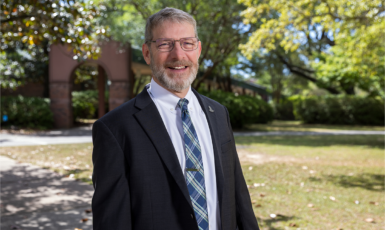 David Fugett stands in a suit on UWF's Pensacola campus in front of the archway.