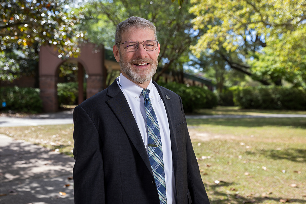 David Fugett stands in a suit on UWF's Pensacola campus in front of the archway.