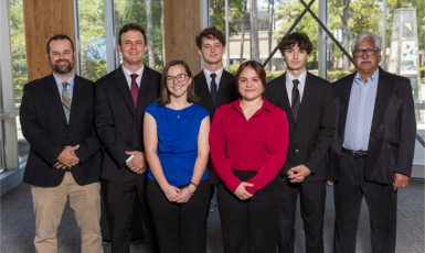 Five students and two professors pose for a photo inside the Lewis Bear Jr. College of Business.