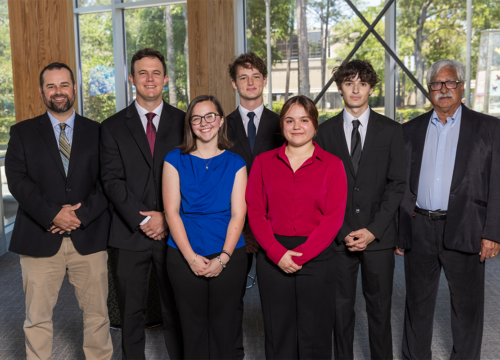 Five students and two professors pose for a photo inside the Lewis Bear Jr. College of Business.