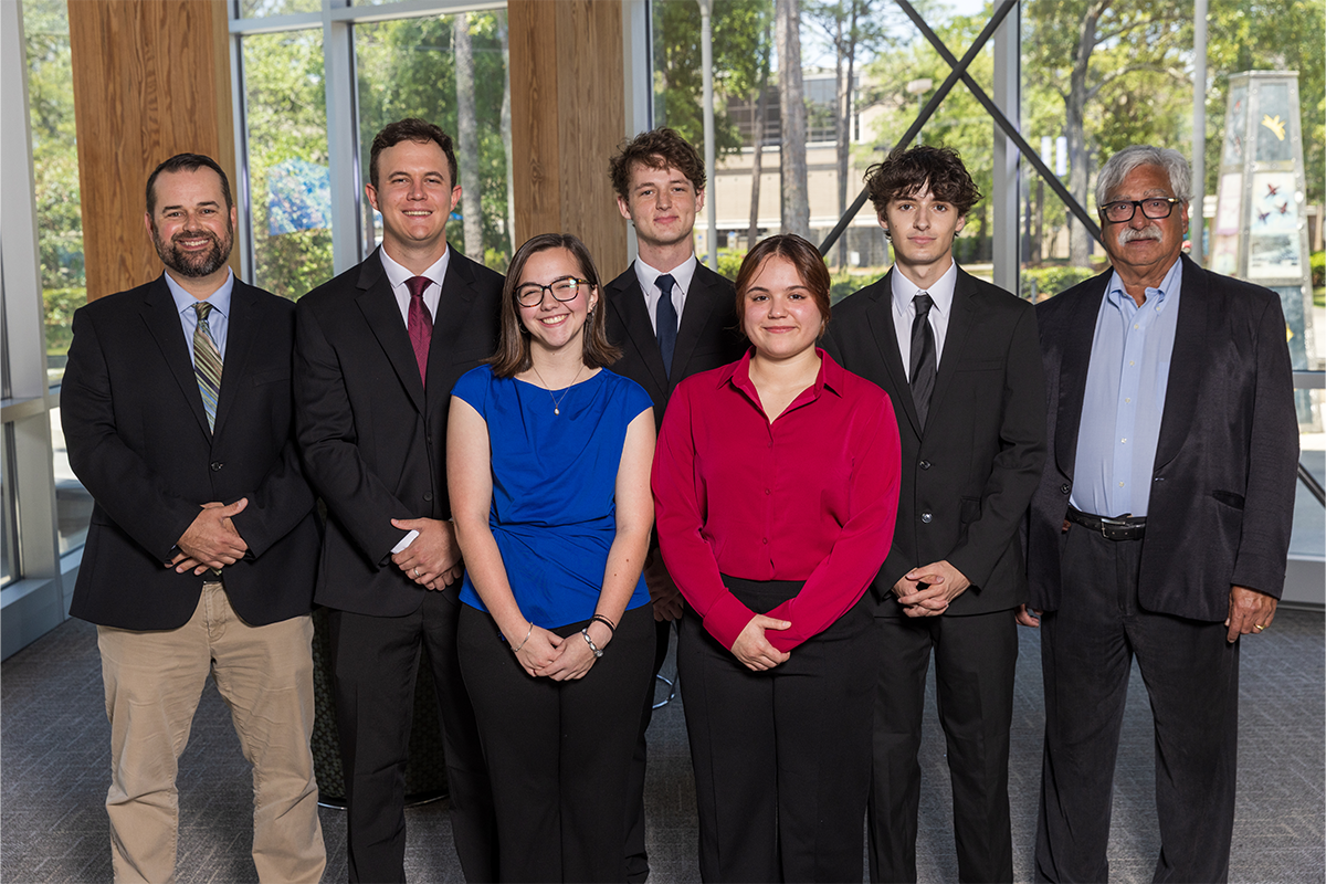 Five students and two professors pose for a photo inside the Lewis Bear Jr. College of Business.