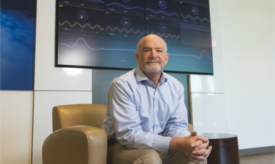 Dr. James Arruda sits in a leather chair in front of a large TV screen with EEG activity displayed.