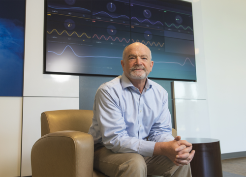 Dr. James Arruda sits in a leather chair in front of a large TV screen with EEG activity displayed.