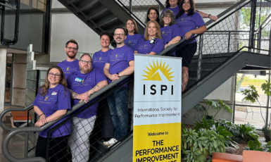 Two professors and nine students pose on a staircase behind a banner that reads: "ISPI International Society for Performance Improvement. Welcome to The Performance Improvement Conference."