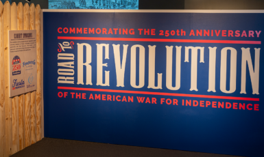 Museum exhibit display wall with text-"Commemorating the 250th Anniversary of the American War for Independence. Road to Revolution.