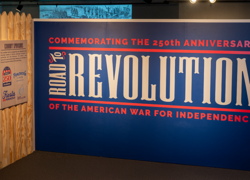 Museum exhibit display wall with text-"Commemorating the 250th Anniversary of the American War for Independence. Road to Revolution.