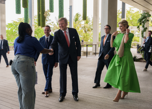 Student shakes hand of king while queen and several others stand in the background watching.