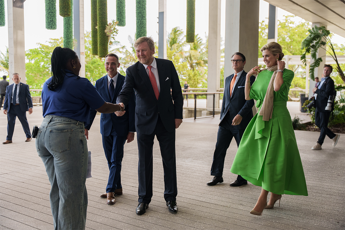 Student shakes hand of king while queen and several others stand in the background watching.