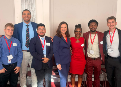 Six students in professional attire pose on either side of Senator Ashley Moody.