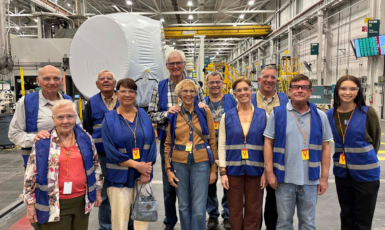 Eleven members of Leisure Learning wearing blue vests pose inside of a factory while on a tour.