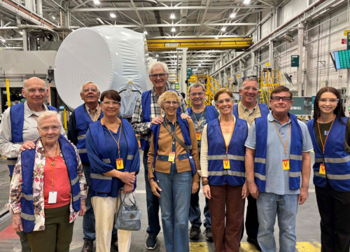Eleven members of Leisure Learning wearing blue vests pose inside of a factory while on a tour.
