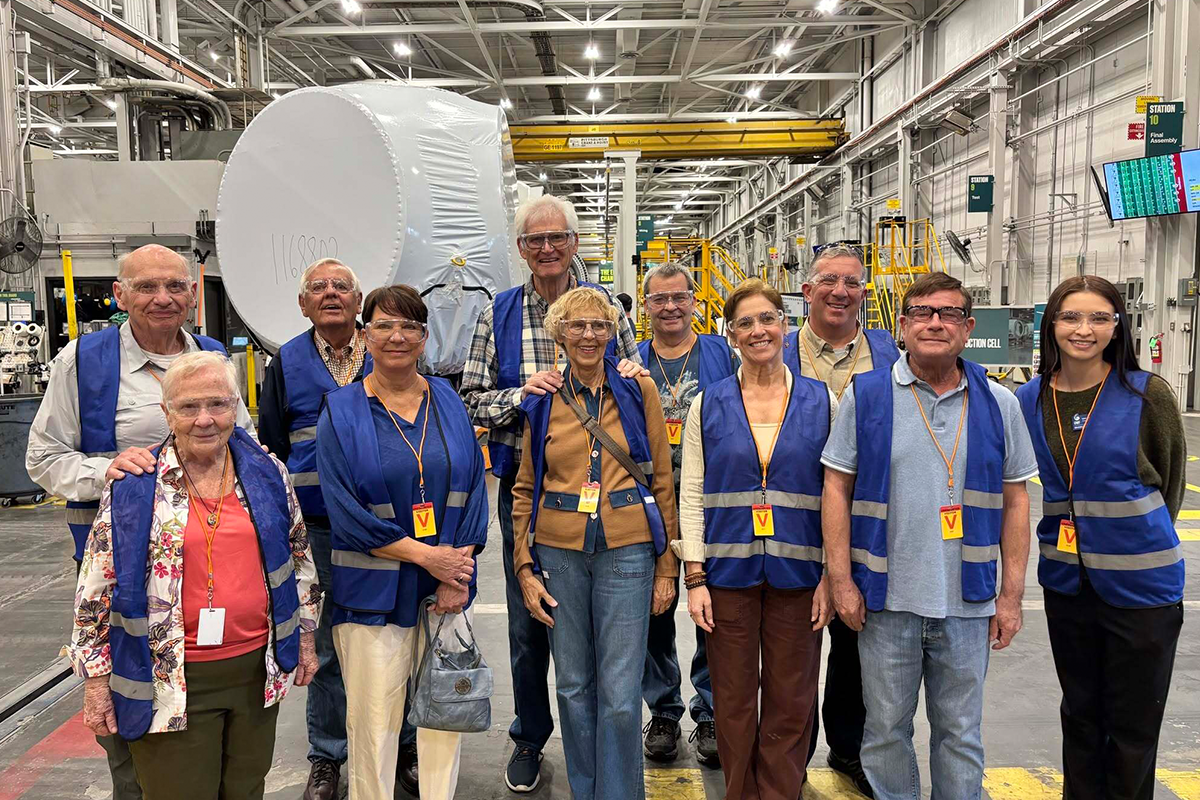 Eleven members of Leisure Learning wearing blue vests pose inside of a factory while on a tour.