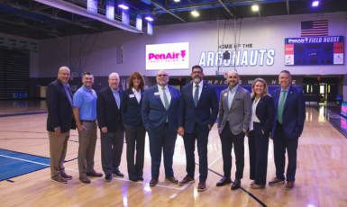 Nine leaders from PenAir Credit Union and UWF stand inside the PenAirField House with signage on the wall behind them that reads. "PenAir Credit Union" and "Home of the Argonauts."