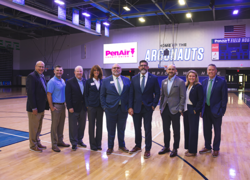 Nine leaders from PenAir Credit Union and UWF stand inside the PenAirField House with signage on the wall behind them that reads. "PenAir Credit Union" and "Home of the Argonauts."