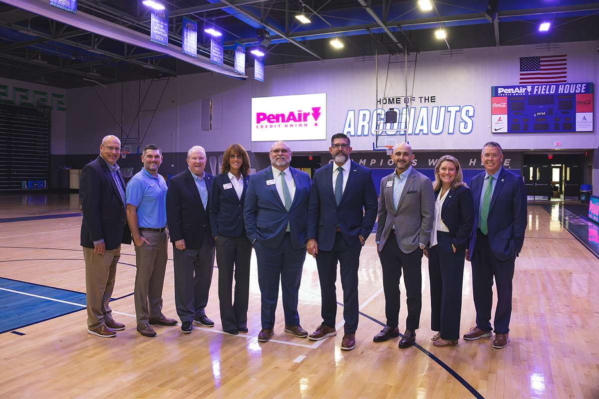 Nine leaders from PenAir Credit Union and UWF stand inside the PenAirField House with signage on the wall behind them that reads. "PenAir Credit Union" and "Home of the Argonauts."