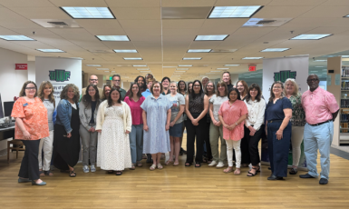 A group of 28 educators stand together in the UWF library.