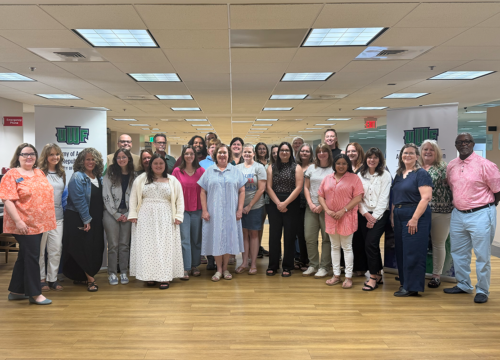 A group of 28 educators stand together in the UWF library.