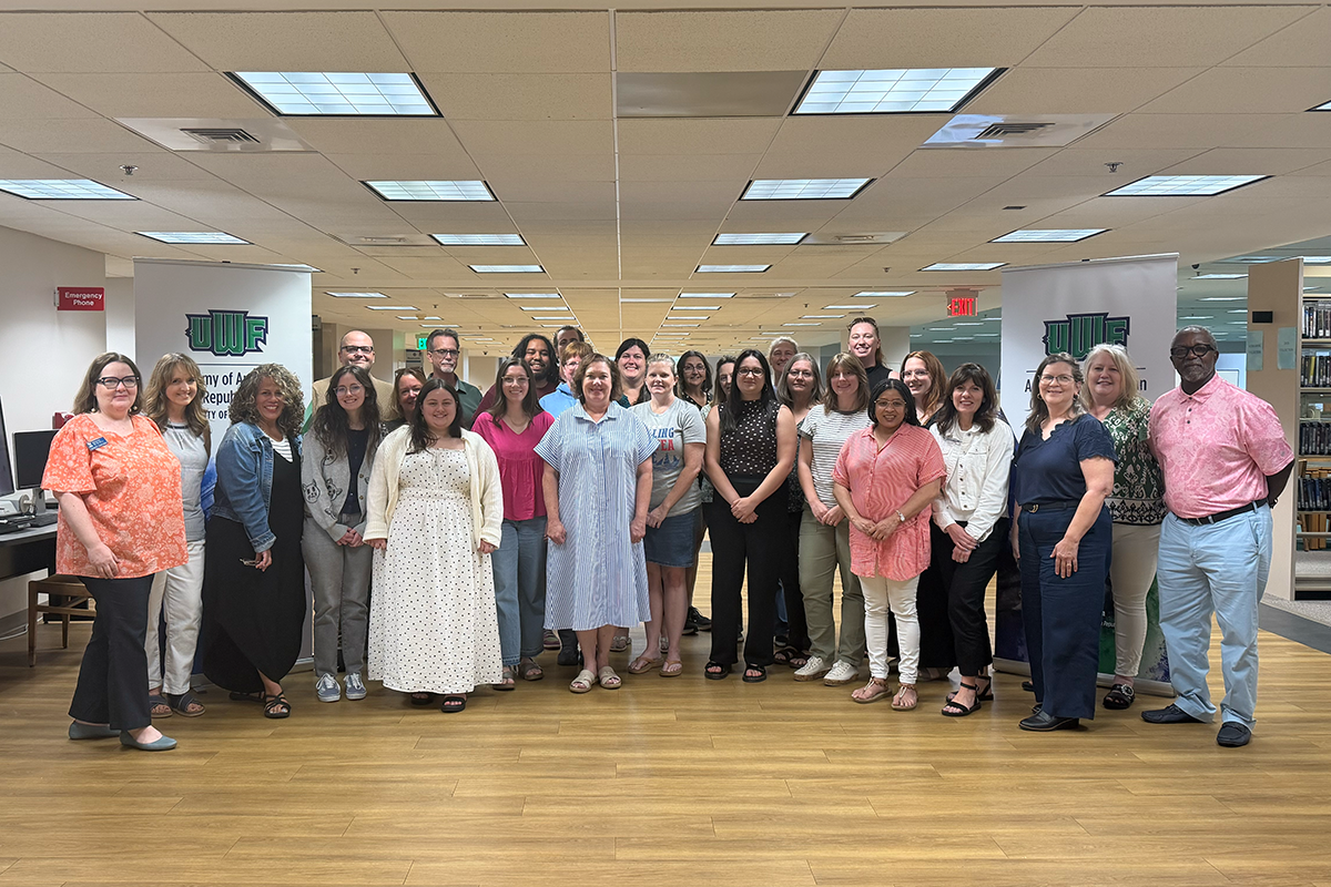 A group of 28 educators stand together in the UWF library.