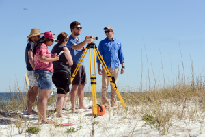 Professor leading an outdoor lesson with 4 students at the beach on how to use a line level to document elevation while mapping.