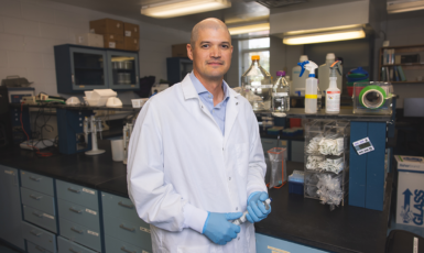 Researcher in white coat stands in science lab holding test tube.