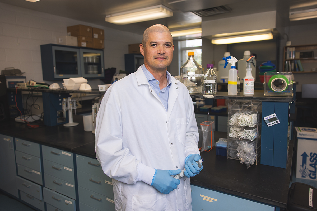Researcher in white coat stands in science lab holding test tube.