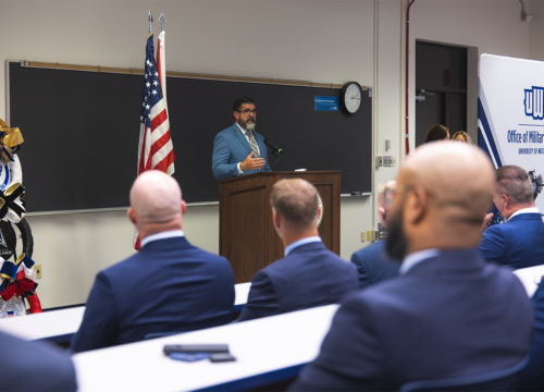 Manny Diaz Jr. speaks at a podium in front of a room of people. Banner on the right says, "UWF Office of Military Services."