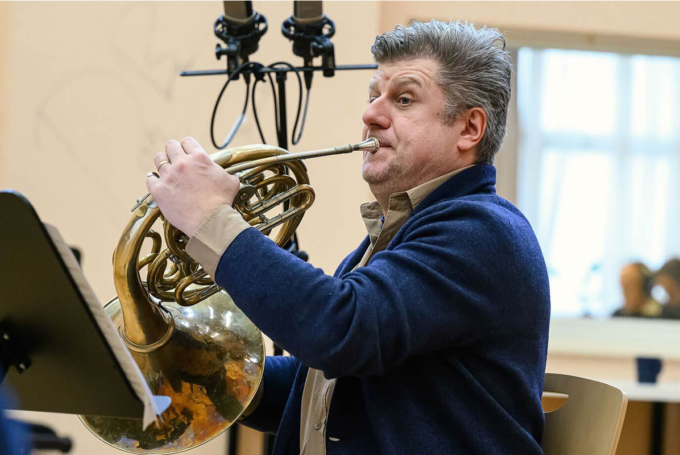 Person plays a french horn in a recording studio.