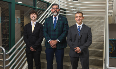 UWF President Manny Diaz Jr. stands between two national merit finalists on the library staircase.