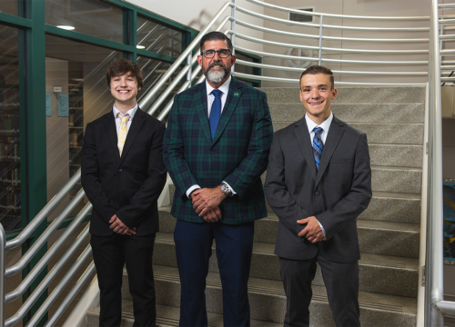 UWF President Manny Diaz Jr. stands between two national merit finalists on the library staircase.