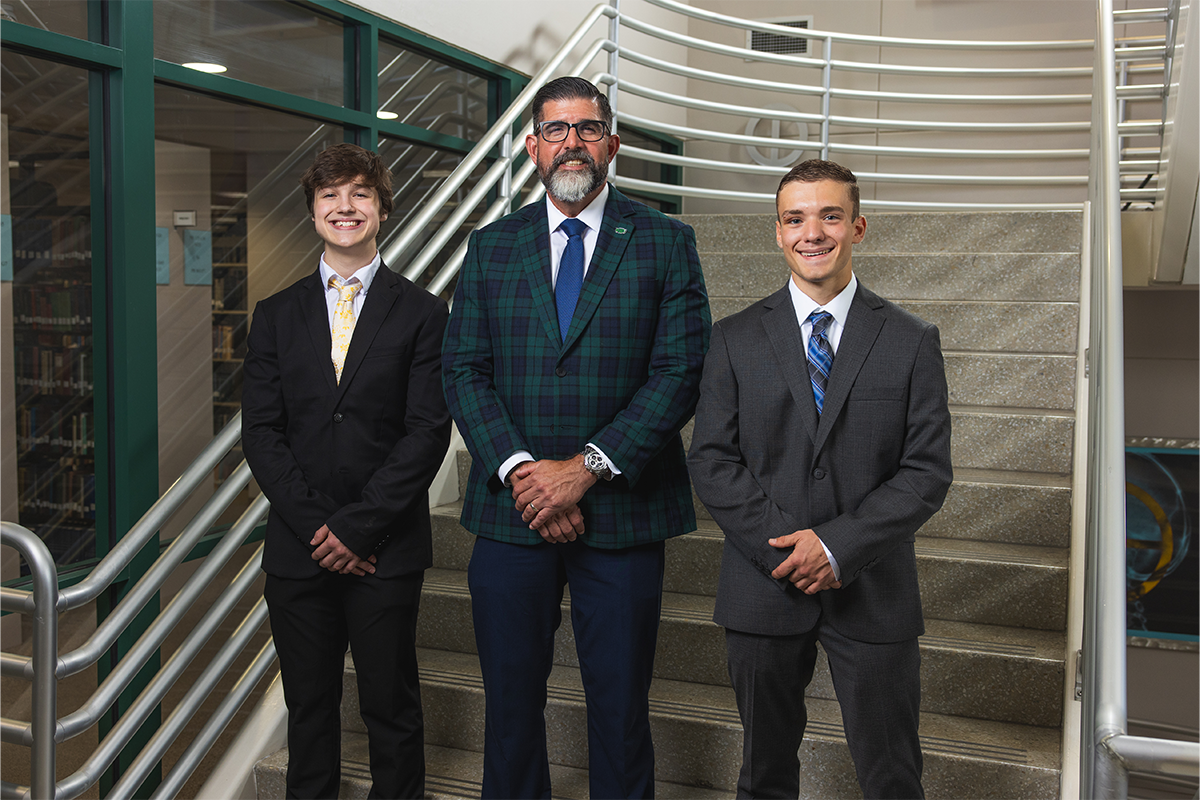 UWF President Manny Diaz Jr. stands between two national merit finalists on the library staircase.