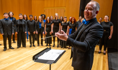 Musical conductor conducts UWF Singers group of students performing on stage.