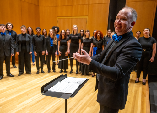 Musical conductor conducts UWF Singers group of students performing on stage.
