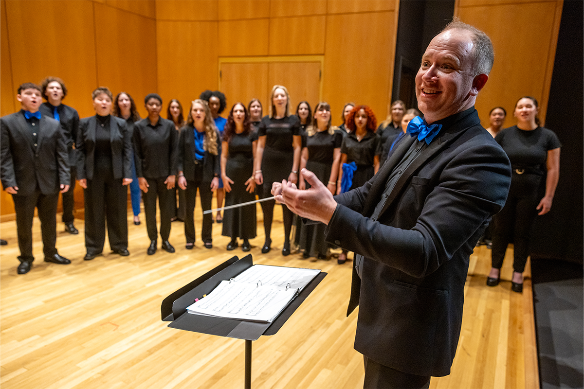 Musical conductor conducts UWF Singers group of students performing on stage.