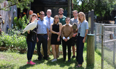 UWF marketing students pose with Wildlife Sanctuary staff. One holds a bird.