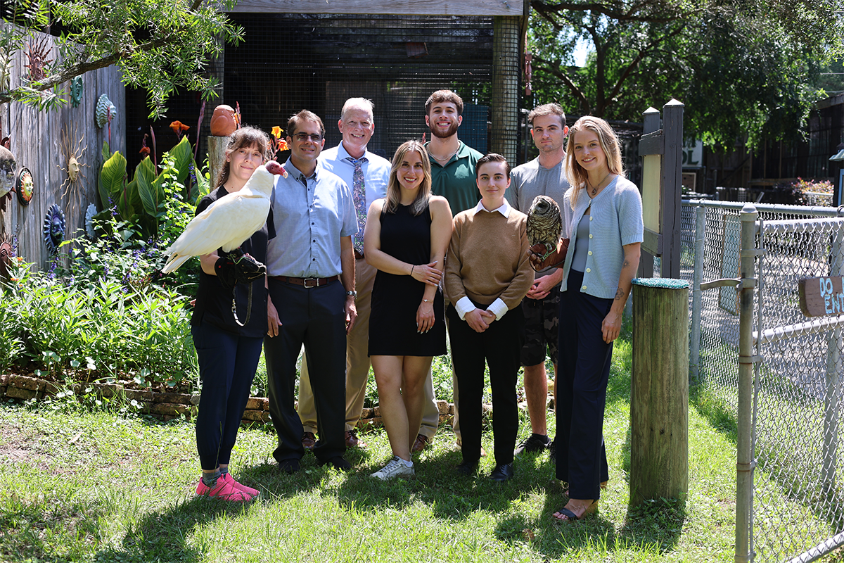 UWF marketing students pose with Wildlife Sanctuary staff. One holds a bird.
