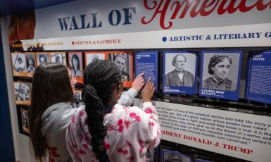 Two middle-school-aged children point at the mobile exhibit's Wall of America featuring photos of historical figures.