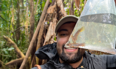 Researcher in a rain jacket holds up a clear bag with fish inside in the Brazilian Amazon.