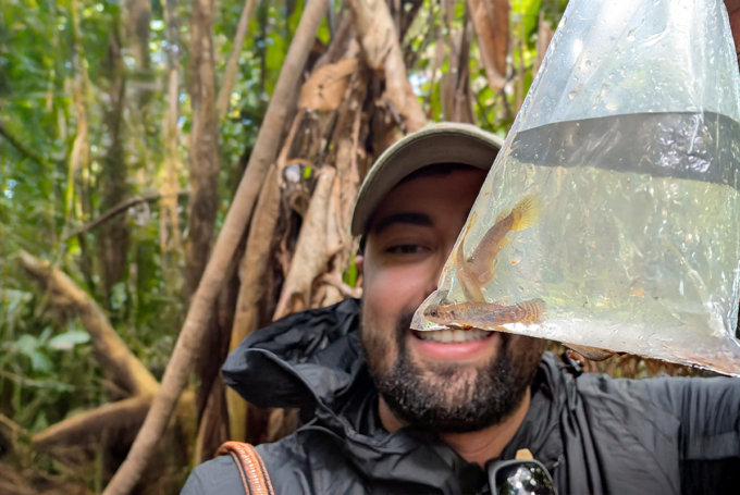 Researcher in a rain jacket holds up a clear bag with fish inside in the Brazilian Amazon.