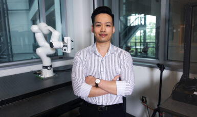 Professor stands with arms crossed in robotics lab.